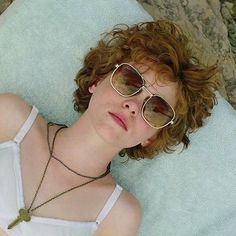 a woman laying down wearing sunglasses and a white tank top with a key necklace on her neck