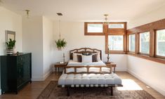 a bed sitting in the middle of a bedroom next to a dresser and two windows