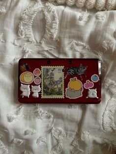 a red tray with pictures on it sitting on a white bed sheet next to a crochet doily