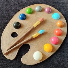 a wooden palette with different colored paints and brushes on it, sitting on a black surface