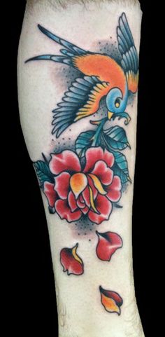 a colorful bird and flower tattoo on the leg, with red flowers in front of it