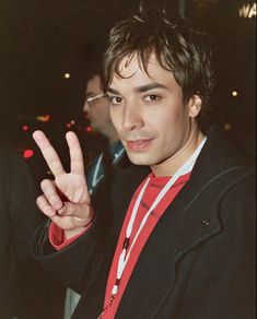 a young man making the peace sign with his hand and wearing a red necktie