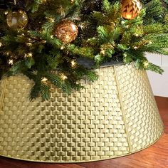 a christmas tree in a gold basket on a wooden floor with ornaments hanging from the top