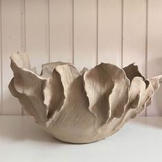 a white bowl with large petals in it sitting on a table next to a wall