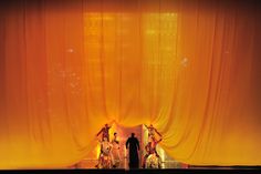 two people standing in front of a stage with orange drapes on the curtained walls