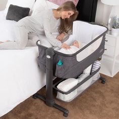 a woman laying in bed next to a baby bassinet and changing table on the floor