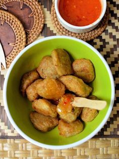 some food is in a green bowl on a table with sauces and spoons