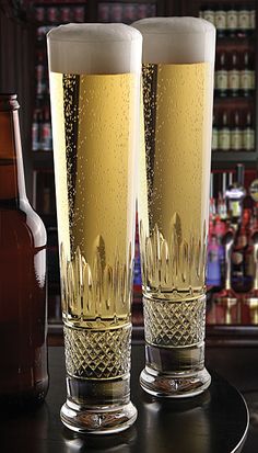 two tall glasses filled with beer sitting on top of a table