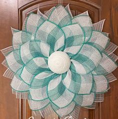 a green and white mesh flower hanging on a wooden door with the words welcome spring written below it