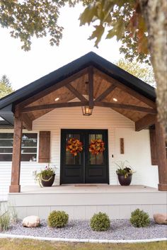 a white house with black doors and two large plants on the front porch, surrounded by trees