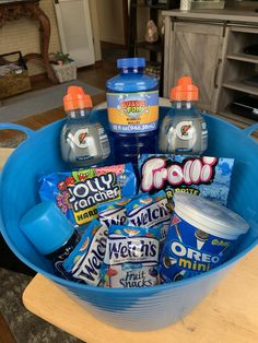 a blue bucket filled with lots of different types of drinks and snacks on top of a wooden table