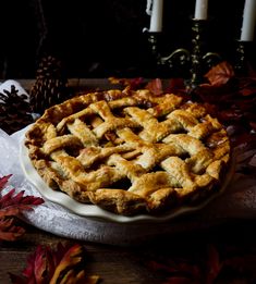 a pie sitting on top of a white plate next to some leaves and pine cones