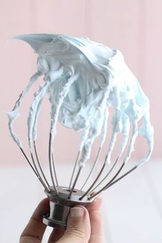 a hand holding a whisk filled with blue icing