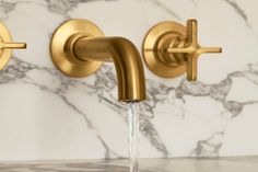 two gold faucets with water running from them on a white marble countertop