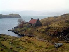 a small house sitting on top of a hill next to a body of water with mountains in the background