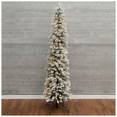 a white christmas tree with snow on it in front of a wooden wall and floor