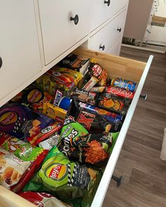 an open drawer filled with snacks on top of a wooden floor next to a white cabinet