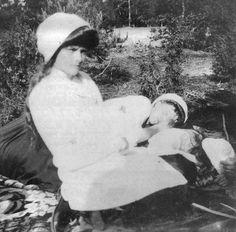 an old black and white photo of a woman holding a baby in her lap while sitting on a blanket