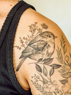 a woman's shoulder with a bird and flowers tattoo on her left upper arm