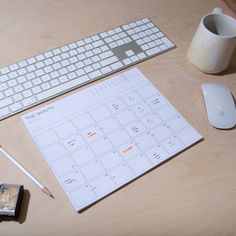 an apple keyboard, mouse and calendar on a wooden table with pencils next to it