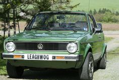 a green car parked on the side of a dirt road next to trees and grass