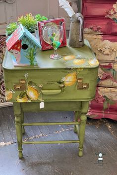 an old green suitcase with bird houses and other items on it's side table