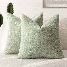 two green pillows sitting on top of a white couch next to a cacti