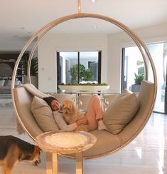 a woman laying on a couch with a dog in front of her and a circular mirror hanging from the ceiling