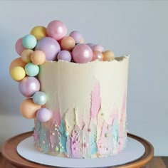 a cake decorated with pastel balloons on top of a wooden table next to a white wall