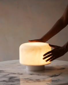 a person reaching for a light on a marble table with their hand over it and touching the base