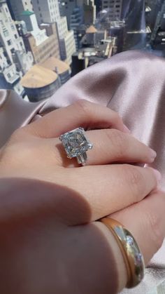 a woman's hand holding an engagement ring in front of a cityscape