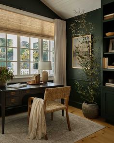 an office with green walls and wooden floors, along with a large window covered in blinds