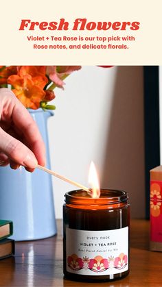 a person lighting a candle on top of a wooden table with flowers in the background