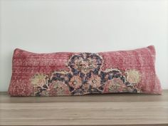 a red and blue decorative pillow sitting on top of a wooden table next to a white wall