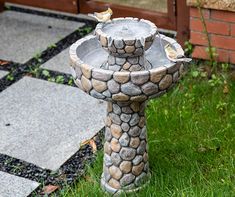 a bird bath sitting on top of a stone pedestal in the grass next to a brick building