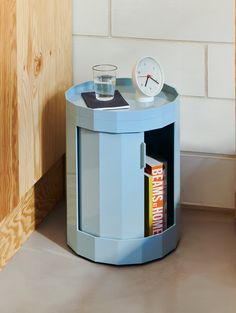 a small blue table with a clock on top and a drink glass in the corner