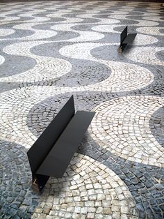 two black benches sitting on top of a cobblestone floor next to each other