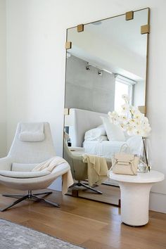 a white chair sitting in front of a mirror on top of a hard wood floor