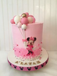 a pink and white cake with minnie mouse on it's side, topped with balloons