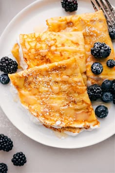 two pieces of french toast on a plate with blueberries and blackberries next to it