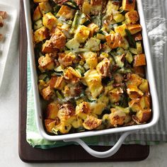 a casserole dish with stuffing and vegetables in it on a tray next to a fork