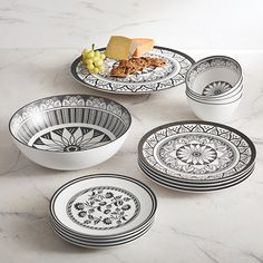 four black and white plates on a marble counter top with cheese, crackers, and grapes