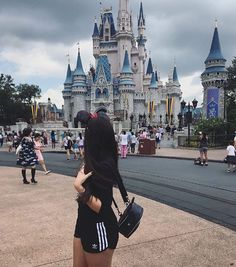 a woman standing in front of a castle with lots of people around her and one person taking a photo