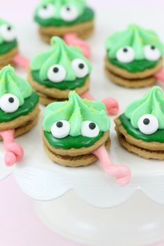 cookies decorated with green icing and googly eyes on a white cake platter