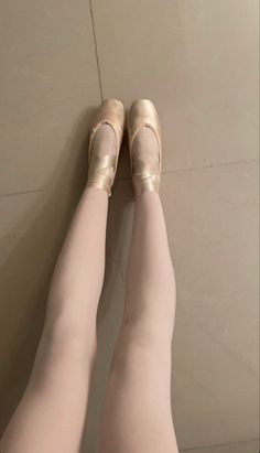 a woman's legs wearing ballet shoes and tights, with her feet on the floor