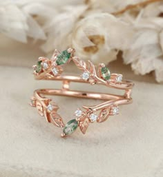 a rose gold ring with green and white stones on the side, surrounded by flowers