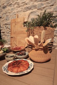 a table topped with plates and bowls filled with food next to a basket full of utensils