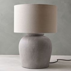 a gray table lamp with a white shade on it's base and a black cord