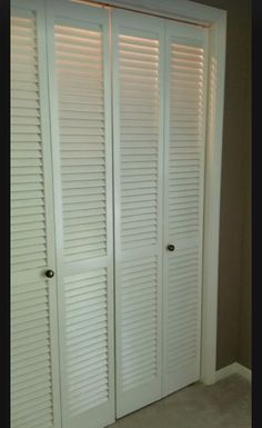 two white closet doors with shutters open in a room that has carpeted flooring and beige walls