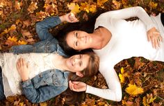 two women laying on the ground with leaves in front of them and looking up at the camera